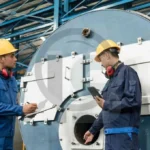 Engenheiros inspecionando caldeira industrial em ambiente fabril.
