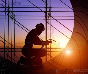 Profissional soldando estrutura metálica ao pôr do sol em canteiro de obras.