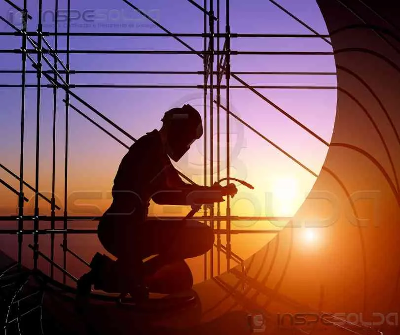 Profissional soldando estrutura metálica ao pôr do sol em canteiro de obras.
