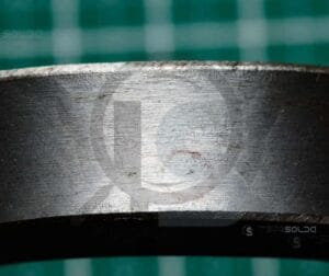 Teste De Dobramento 24 Amostra metálica com marcações visíveis após teste de dobramento, destacando falhas ou trincas no material.