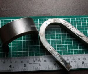 Teste De Dobramento 22 Peças metálicas dobradas sobre superfície quadriculada, representando resultados de testes de dobramento em soldagem.