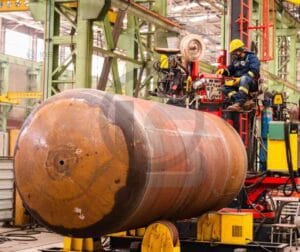 Cilindro metálico em processo de soldagem a arco submerso em ambiente industrial.
