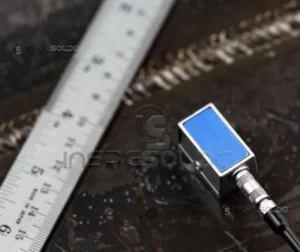 Soldagem Por Ultrassom 29 Sonda de ultrassom para inspeção de soldagem ao lado de uma régua metálica sobre uma superfície metálica.