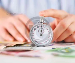 Mãos segurando um cronômetro sobre uma mesa com documentos, simbolizando otimização de tempo na produção.