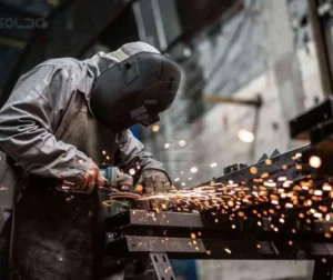 Trabalhador realizando análise de superfície metálica com faíscas visíveis.