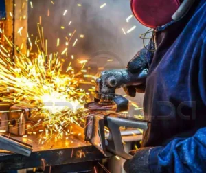 Soldador trabalhando com metal, gerando faíscas no processo de soldagem.
