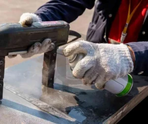 Inspeção com partículas magnéticas sendo aplicada em uma peça metálica para detecção de descontinuidades.
