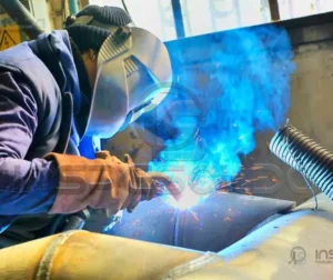 Soldador realizando soldagem com arco elétrico e proteção gasosa.