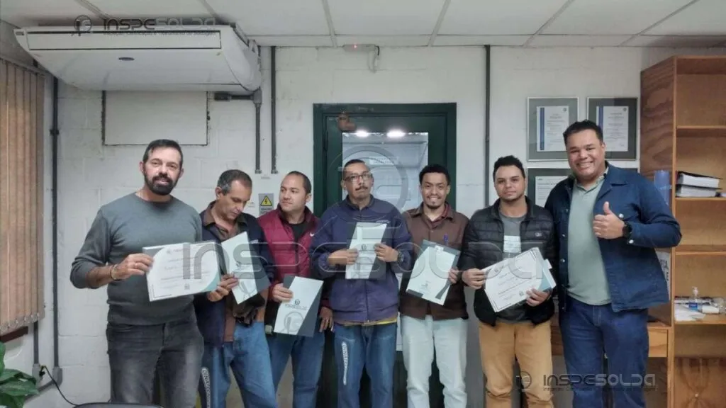 home-treinamento-de-soldagem-in-company Colaboradores exibem certificado de conclusão de treinamento em soldagem, acompanhados do instrutor.