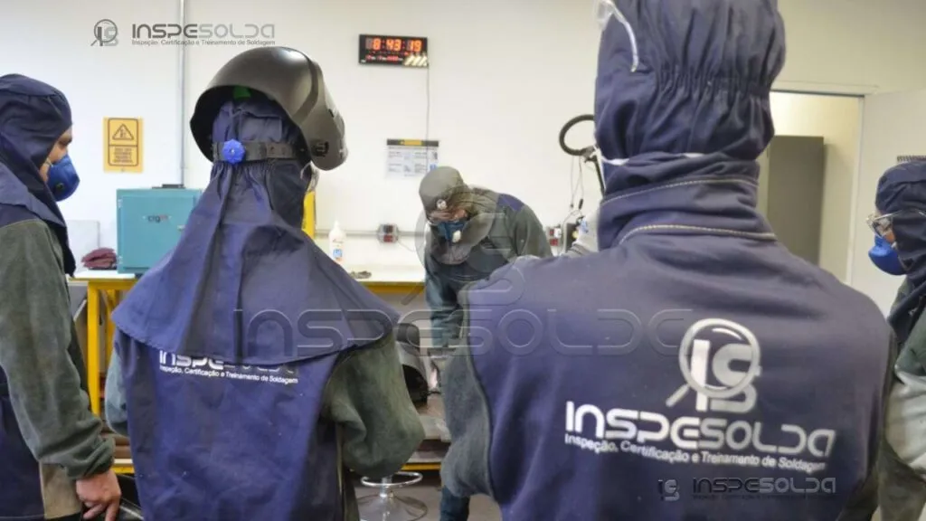 home-treinamento-de-soldagem-pratico-eletrodo Profissionais em treinamento de soldagem eletrodo revestido, usando EPIs e com supervisão técnica.