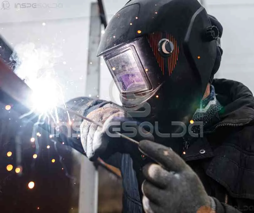 Soldador com máscara realizando inspeção e solda técnica.
