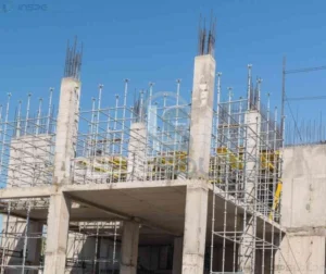 Estrutura de concreto armado em construção, com pilares e armações metálicas visíveis.