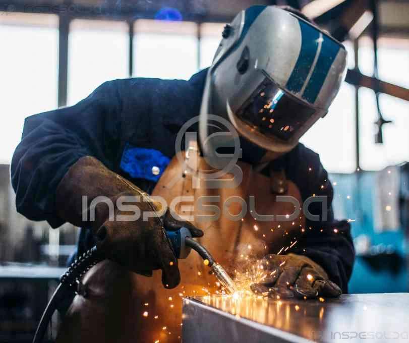 Soldador realizando soldagem a arco com EPI completo, enquanto faíscas brilham, representando a precisão técnica e a habilidade manual exigida nesse processo.