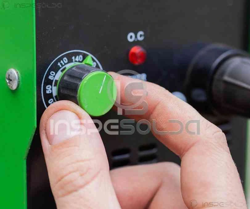 Mão ajustando o painel de controle de um equipamento de soldagem manual, representando o início do processo artesanal.